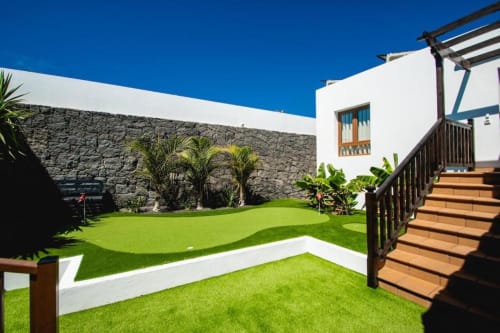 Patio de Villa Cavendish en Playa Blanca con césped exuberante, muros de piedra, edificio blanco, plantas tropicales y detalles de madera