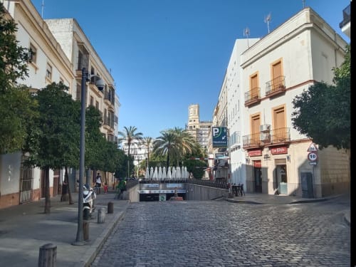 Plaza histórica en Jerez de la Frontera con arquitectura colonial, palmeras y torre de iglesia al fondo