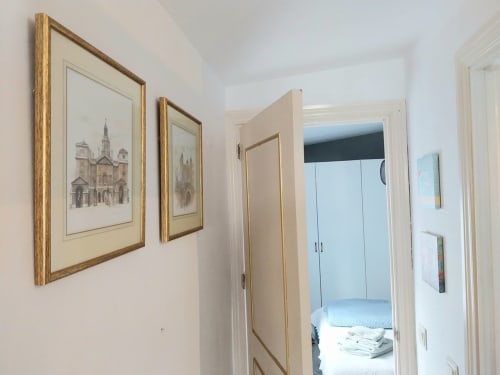 Pasillo luminoso en apartamento de Jerez con láminas arquitectónicas enmarcadas y puerta del dormitorio
