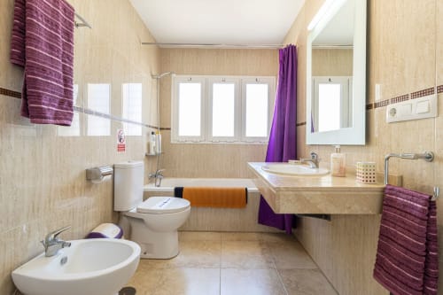 Baño moderno del apartamento Top Home Integra en Jerez de la Frontera con doble lavabo, bañera y detalles en púrpura
