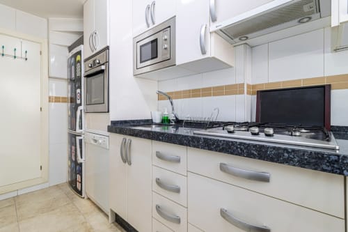 Cocina moderna con gabinetes blancos, encimera de granito oscuro, estufa de gas y electrodomésticos de acero inoxidable en Jerez de la