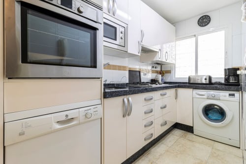 Cocina moderna con gabinetes color crema, encimera de granito negro, electrodomésticos de acero inoxidable y lavadora en Top Home