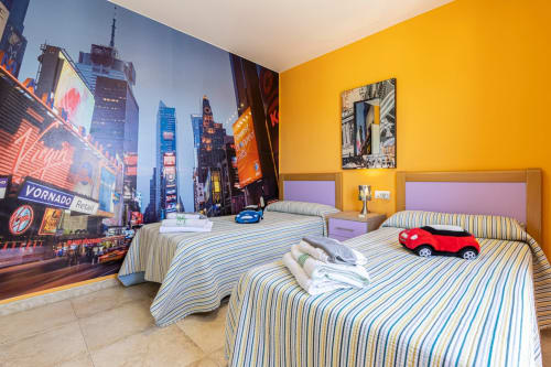 Dormitorio amarillo brillante en apartamento Top Home Integra de Jerez de la Frontera con mural de Times Square, camas rayadas y juguete