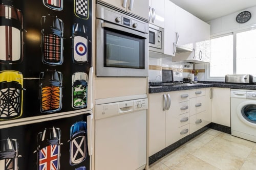 Cocina moderna con arte mural temático de autos retro, armarios color crema y electrodomésticos en apartamento de Jerez