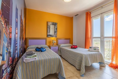 Dormitorio infantil luminoso en Top Home Integra con camas dobles, detalles naranjas y vistas a la ciudad de Jerez de la Frontera, España