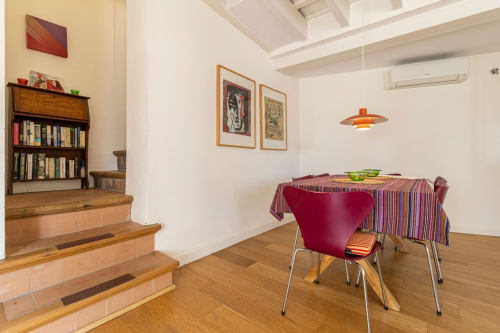 Comedor moderno en apartamento de Jerez con suelos de madera, silla roja, mantel a rayas, estantería y luminarias colgantes