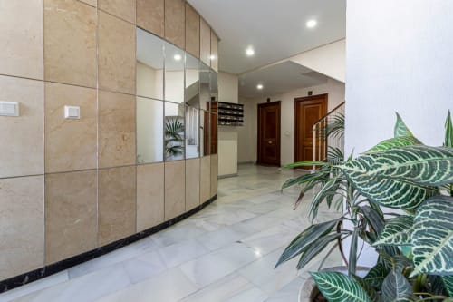Recepción moderna del Top Home Integra en Jerez de la Frontera con paredes de mármol, mamparas de cristal y plantas en macetas