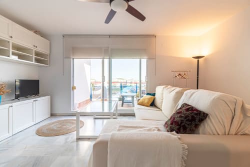 Moderno salón de apartamento con sofá crema, TV, cocina americana y vistas al balcón en Jerez de la Frontera