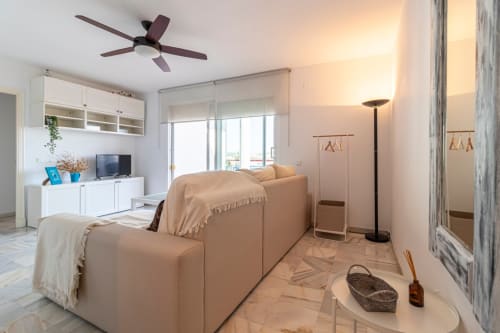 Moderno salón de apartamento en Top Home Integra, Jerez de la Frontera, con sofá beige, ventilador de techo y vistas a la sierra