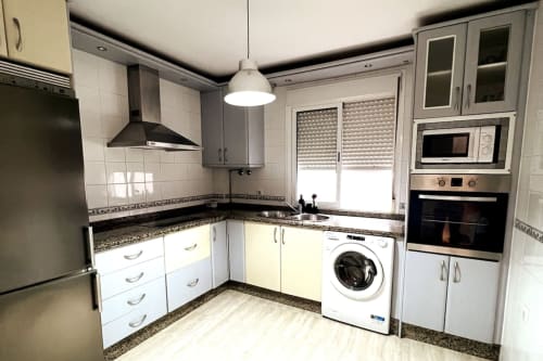 Cocina moderna del apartamento Top Home Integra en Jerez de la Frontera con muebles blancos, encimeras de granito y acero inoxidable