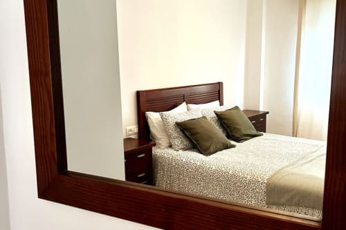 Dormitorio del apartamento Top Home Integra en Jerez de la Frontera con cama de madera, ropa de cama estampada y reflejo en espejo