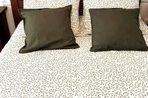 Cama con dos almohadas verde oliva sobre ropa de cama estampada en el apartamento Top Home Integra de Jerez de la Frontera