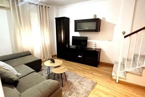 Moderno salón del apartamento Top Home Integra en Jerez de la Frontera con sofá gris, módulo TV negro y suelos de madera