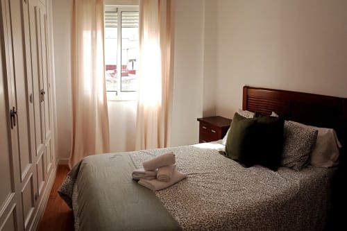 Dormitorio luminoso en apartamento Top Home Integra en Jerez de la Frontera con cama de madera, ropa de cama estampada y vista al jardín