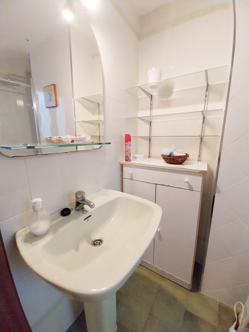 Baño moderno con lavamanos pedestal, espejo, estantería y accesorios blancos en apartamento Top Home Integra en Jerez de la