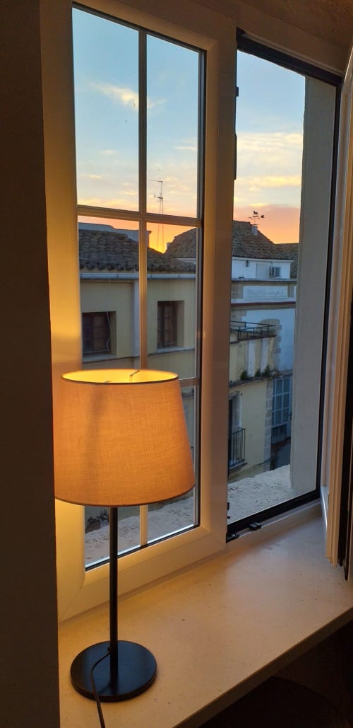 Lámpara de pie junto a la ventana del apartamento Top Home Integra en Jerez de la Frontera, con vistas al atardecer de edificios históricos