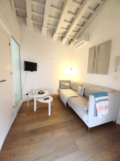 Apartamento estudio moderno en Top Home Integra de Jerez de la Frontera con sofá, mesas auxiliares blancas, TV y vigas de madera vista