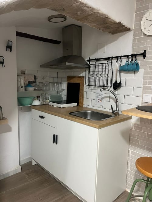 Cocina moderna con muebles blancos, encimera de madera, fregadero de acero inoxidable, campana negra y estantería abierta en Top Home