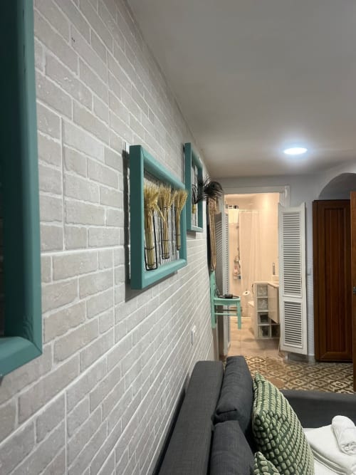 Interior moderno de apartamento en Top Home Integra, Jerez de la Frontera, con pared de ladrillo blanco, obra de arte con marco turquesa y