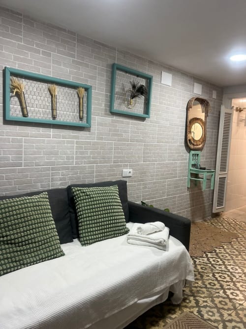 Dormitorio moderno en apartamento Top Home Integra en Jerez con cuadros artísticos de marco turquesa, sofá negro con cojines verdes