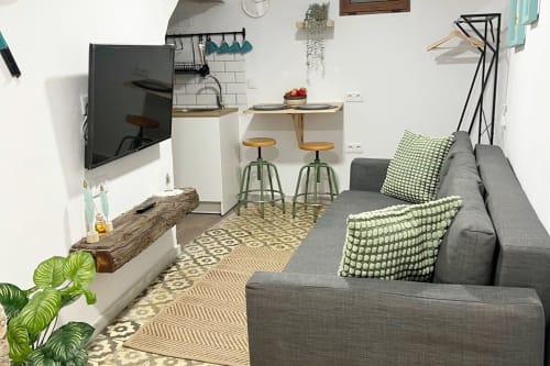 Moderno apartamento estudio en Jerez de la Frontera con sofá gris, cocineta, TV y decoración en tonos verdes