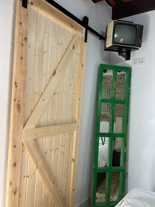 Habitación rústica con puerta de granero en pino natural, gabinete espejo verde y televisor vintage en el hotel Top Home Integra de Jerez