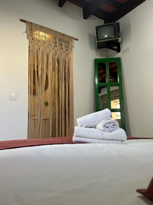 Acogedora habitación en Top Home Integra, Jerez de la Frontera con ropa de cama blanca, cortinas de macramé, espejo verde y