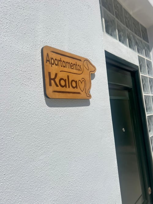 Cartel de madera de Kalam Apartamentos en pared blanca con puerta verde en Jerez de la Frontera
