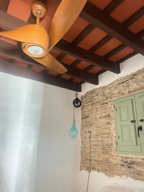 Ventilador de techo de madera con vigas expuestas y lámpara colgante turquesa en apartamento de Jerez