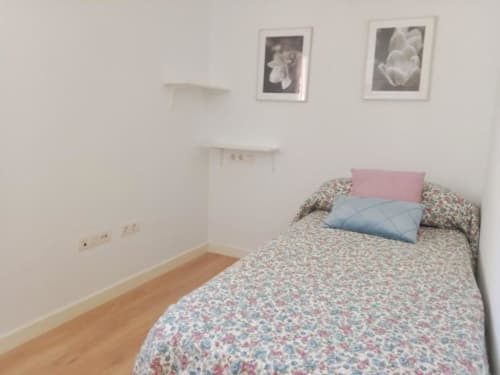 Acogedora habitación en apartamento Top Home Integra de Jerez de la Frontera con ropa de cama floral, almohadas rosas y cuadros enmarcados en la pared