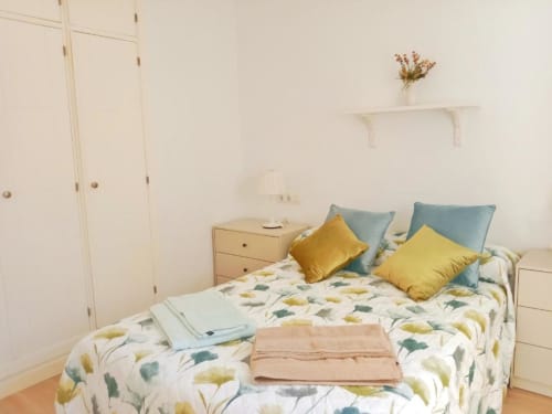 Habitación luminosa en Top Home Integra en Jerez de la Frontera con ropa de cama floral, almohadas amarillas y azules, muebles blancos y