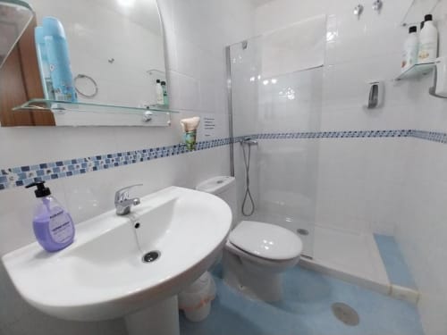 Cuarto de baño moderno con azulejos blancos, cenefa de mosaico azul, lavabo, inodoro y ducha en apartamento Top Home Integra en Jerez de la