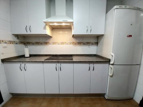 Cocina moderna en apartamento Top Home Integra, Jerez de la Frontera, con gabinetes blancos, encimera de granito y acero inoxidable