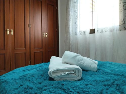 Cama turquesa con toallas y almohadas blancas en apartamento Top Home Integra, Jerez de la Frontera