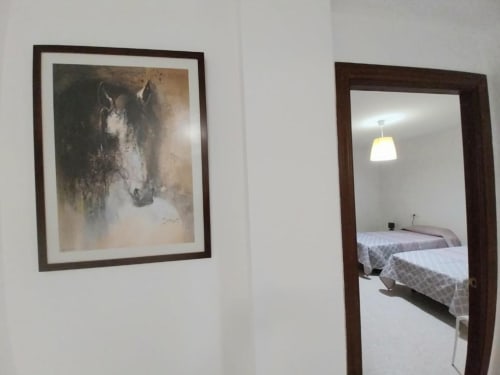 Pasillo de dormitorio con cuadros de caballos enmarcados y espejo reflejando camas en apartamento Top Home Integra en Jerez de la Frontera