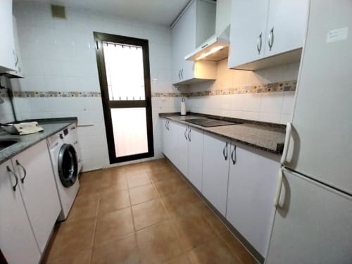 Cocina moderna de galera con muebles blancos, encimeras oscuras y suelos de terracota en Top Home Integra, Jerez de la