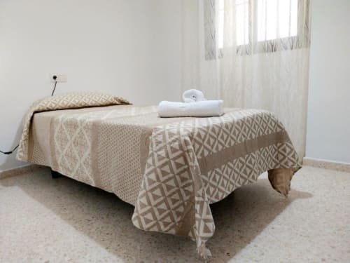Dormitorio minimalista en apartamento Top Home Integra de Jerez de la Frontera con cama individual, ropa de cama beige y vista al jardín