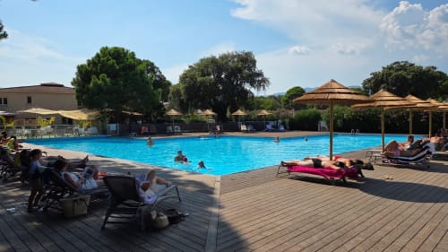 Piscine de l'hôtel Alma Rossa à Lecci avec des clients se baignant et se détendant sur la terrasse en bois entourée d'arbres