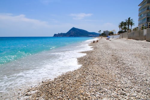 Pebbly beach at Lemon Hostel Altea with turquoise Mediterranean Sea and rocky island mountain backdrop