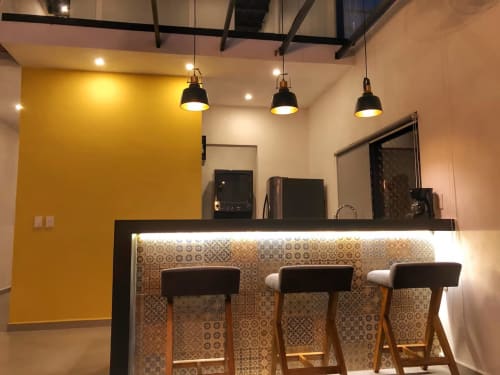 Modern loft kitchen bar with three stools at Anita Ocean View Puerto Vallarta, featuring yellow accent wall and pendant