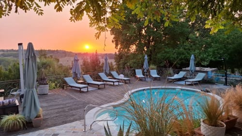 Sunset view of Maison Mûrier's pool deck in Fayssac with loungers, umbrellas, and countryside landscape