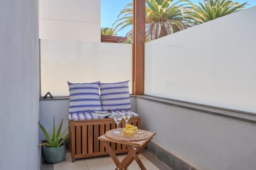 Acogedor balcón en Villa Cavendish con banco acolchado a rayas, mesita, maceta y palmeras vistas en Playa