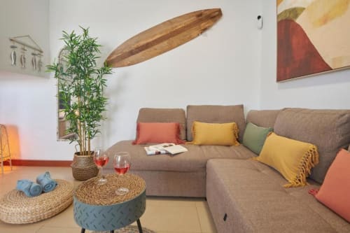 Amplia sala de estar en Villa Cavendish con sofá beige, cojines coloridos, planta de bambú y tabla de surf decorativa