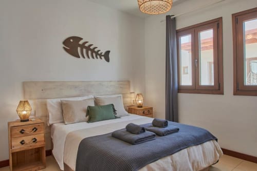 Dormitorio luminoso en Villa Cavendish, Playa Blanca, con cama de madera, arte de peces en la pared y vistas al océano