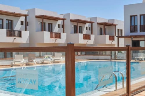 Piscina del resort Villa Cavendish con casas mediterráneas blancas y tumbonas de madera en Playa Blanca, España