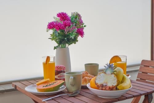 Desayuno en el balcón de Villa Cavendish con frutas tropicales, pastelería, jugo, flores y vista al jardín en Playa Blanca