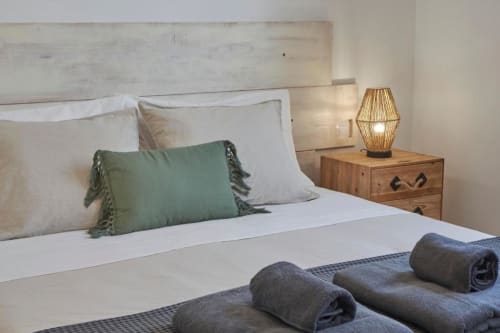 Dormitorio moderno en Villa Cavendish con ropa de cama blanca, almohada verde, mesita de noche de madera y lámpara tejida