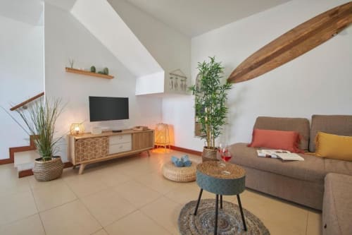 Moderno salón de apartamento en Villa Cavendish, Playa Blanca, con sofá gris, mueble TV de madera, plantas y luz natural