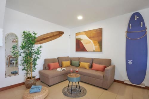 Sala moderna Villa Cavendish, Playa Blanca con sofá beige, cojines coloridos, decoración de tabla de surf y vista al jardín