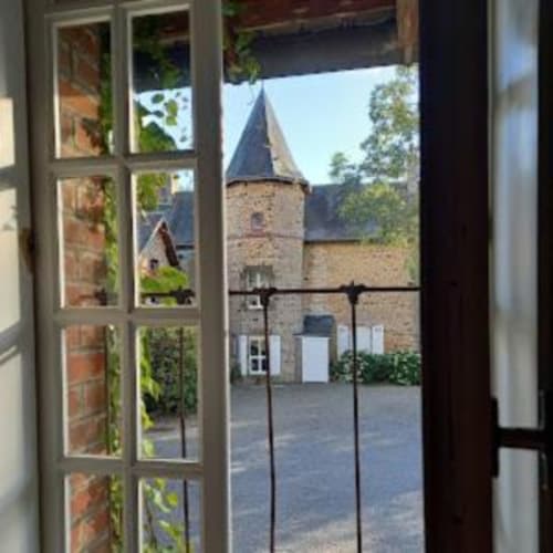 Medieval stone tower with cone roof viewed through open French doors at Le Petit Lustucru, Avranches